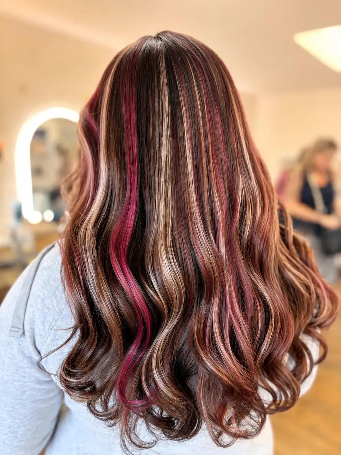 Long wavy dimensional chocolate hair with blonde and magenta ribbons in a salon